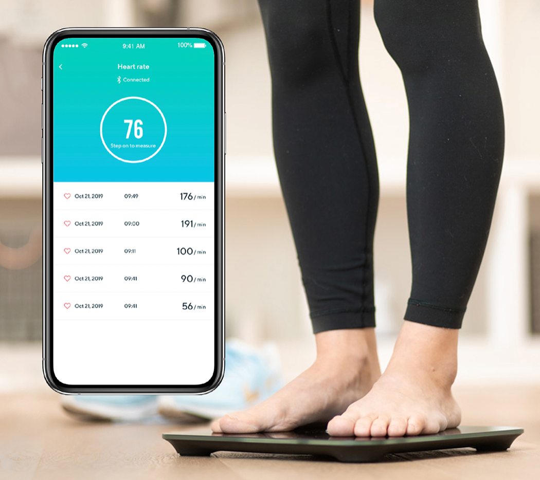 Person standing on the Wyze scale with a phone screen showing their heart rate stats in the Wyze app