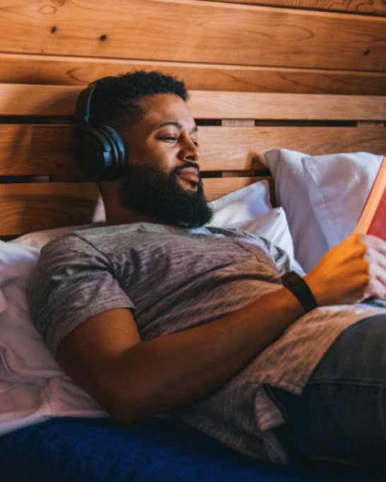 Person relaxing in bed with a book while wearing wyze headphones