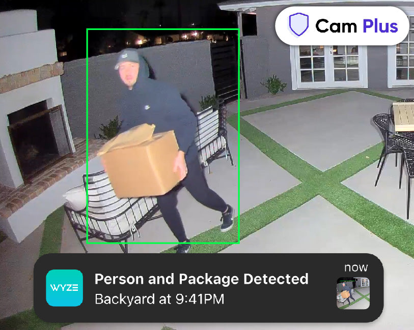 Man carrying packages away from the house during the night with the lights shining directly at him. Phone notification overlay of alert about the camera's detection.
