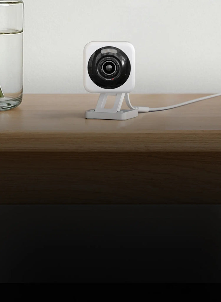 White security camera on a wooden surface with a glass of water in the background