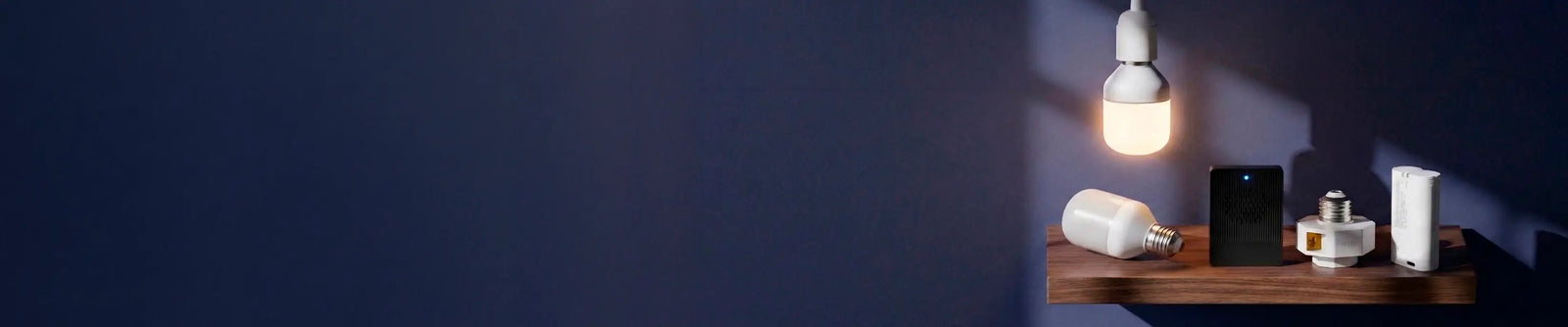 Small wooden shelf with a light bulb, phone, and other items against a dark wall.