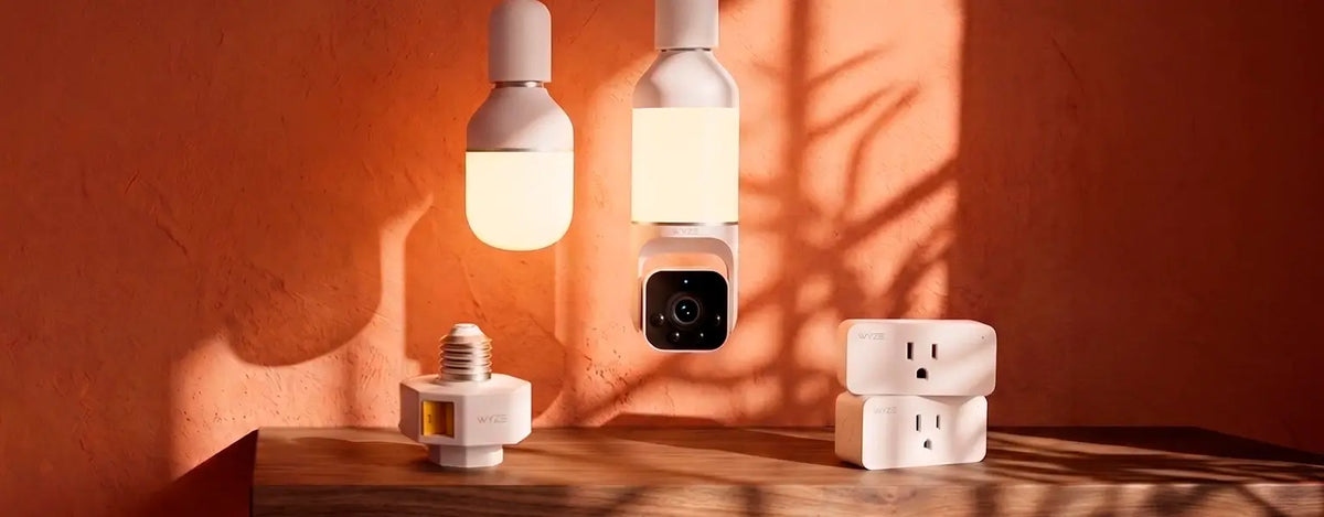 Smart home devices including light bulbs and a camera on a wooden surface with an orange wall background.