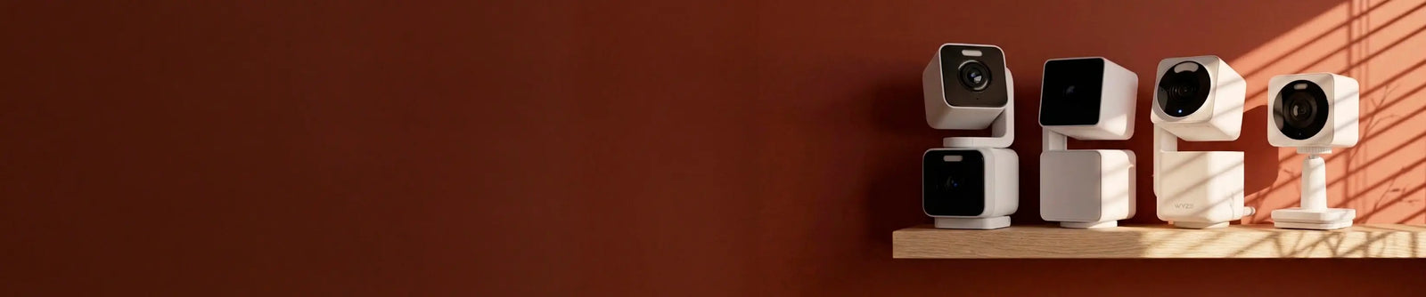 Four security cameras on a wooden shelf against a red-brown wall.