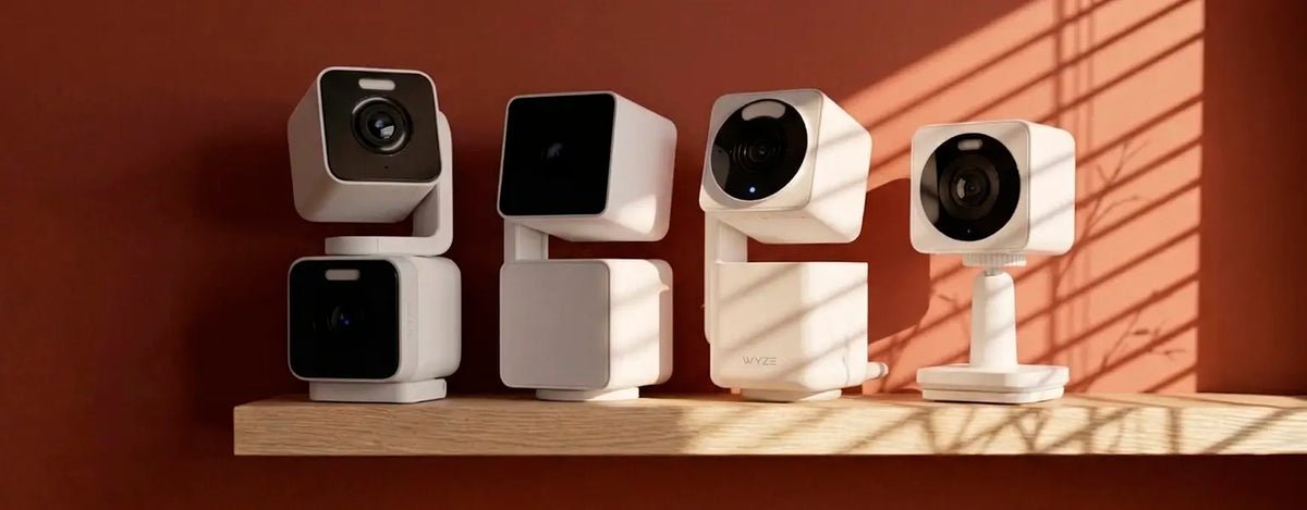 Four white security cameras with black lenses on a wooden shelf against a red-brown wall.
