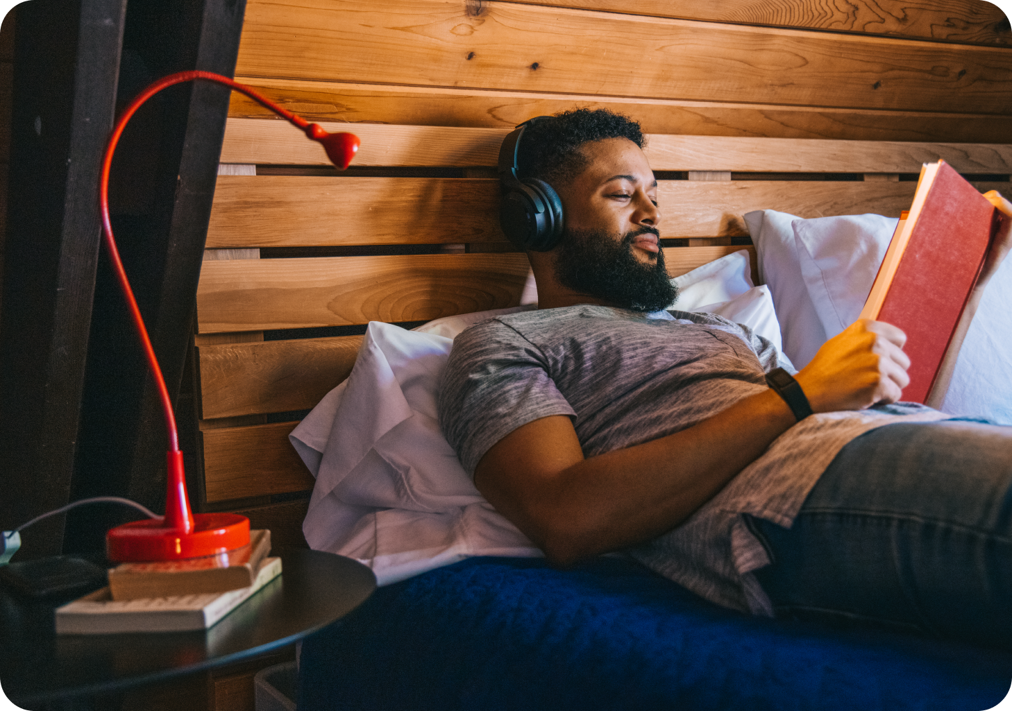 Person laying in bed, reading a book wearing wyze headphones
