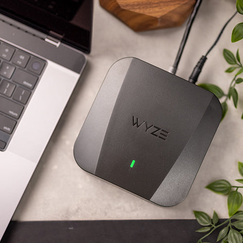 A Wyze Mesh Router Pro on a desk beside a laptop.