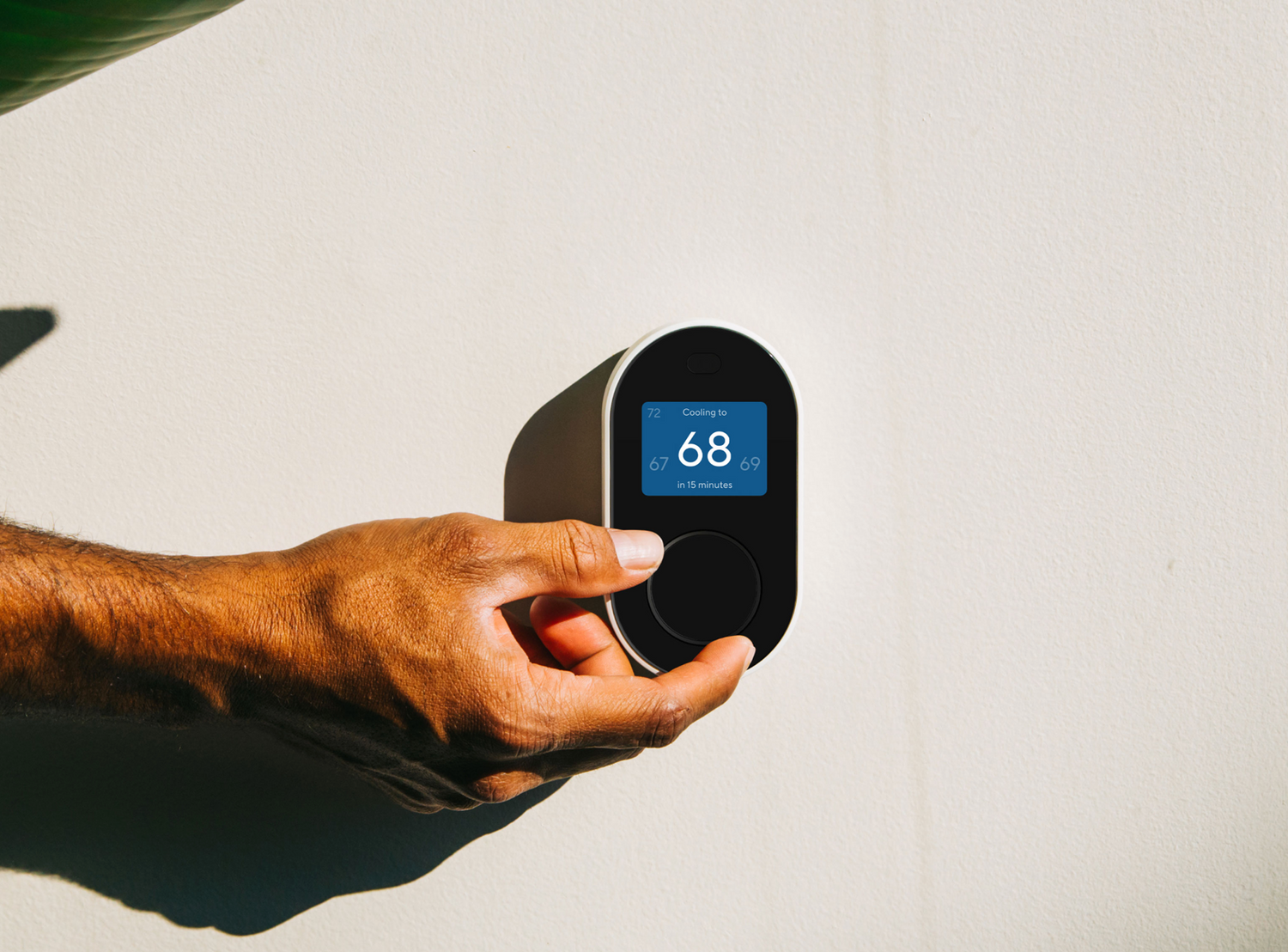 Hand adjusting the Wyze Thermostat unit that is mounted on a wall.