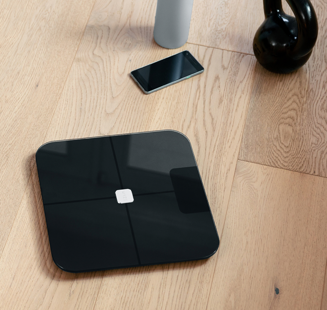 Wyze Scale on wood floor with phone and exercising tools in view