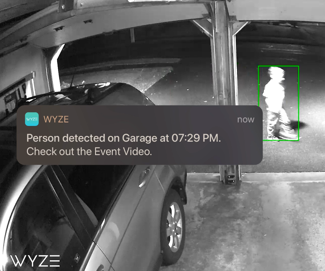 Image of a child walking past garage with motion detection alert from Wyze app on screen.