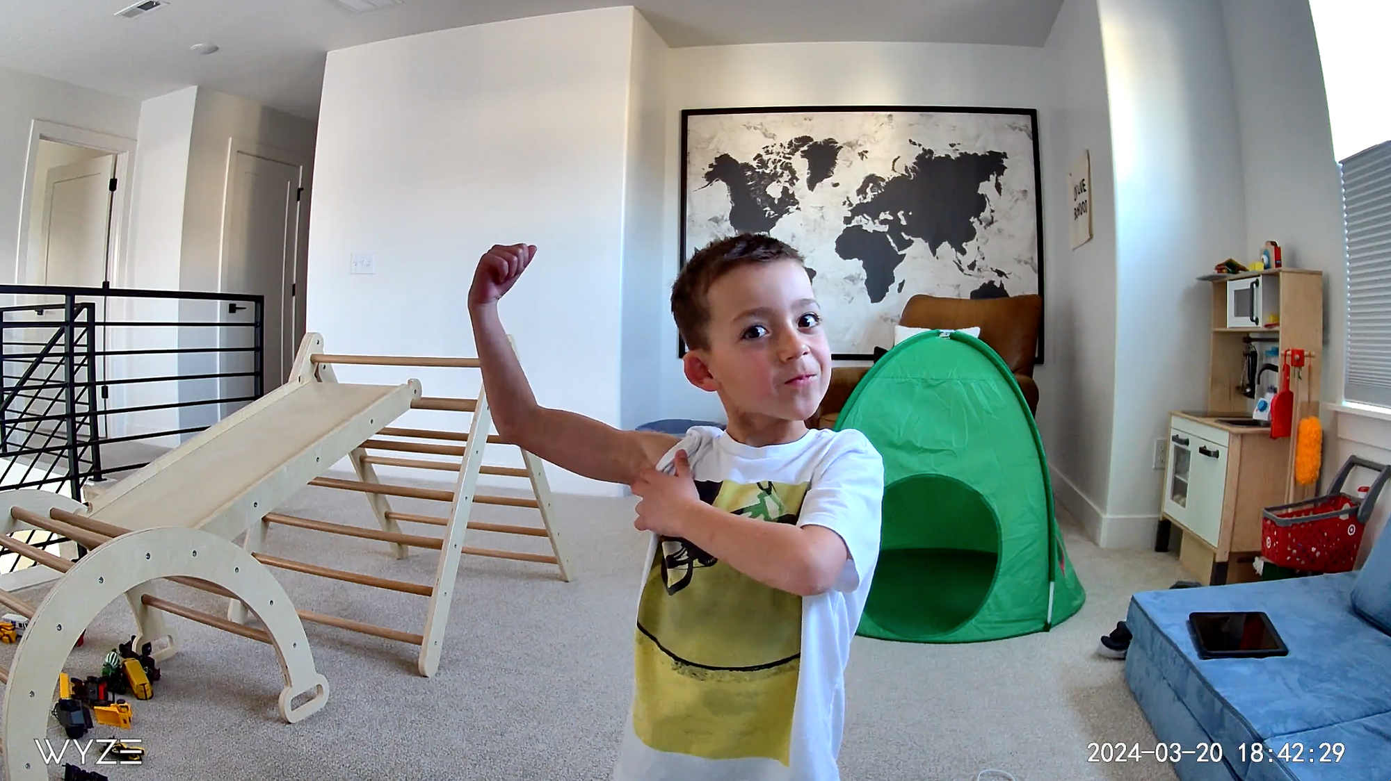 A young boy is flexing his arm in front of a map of the world.