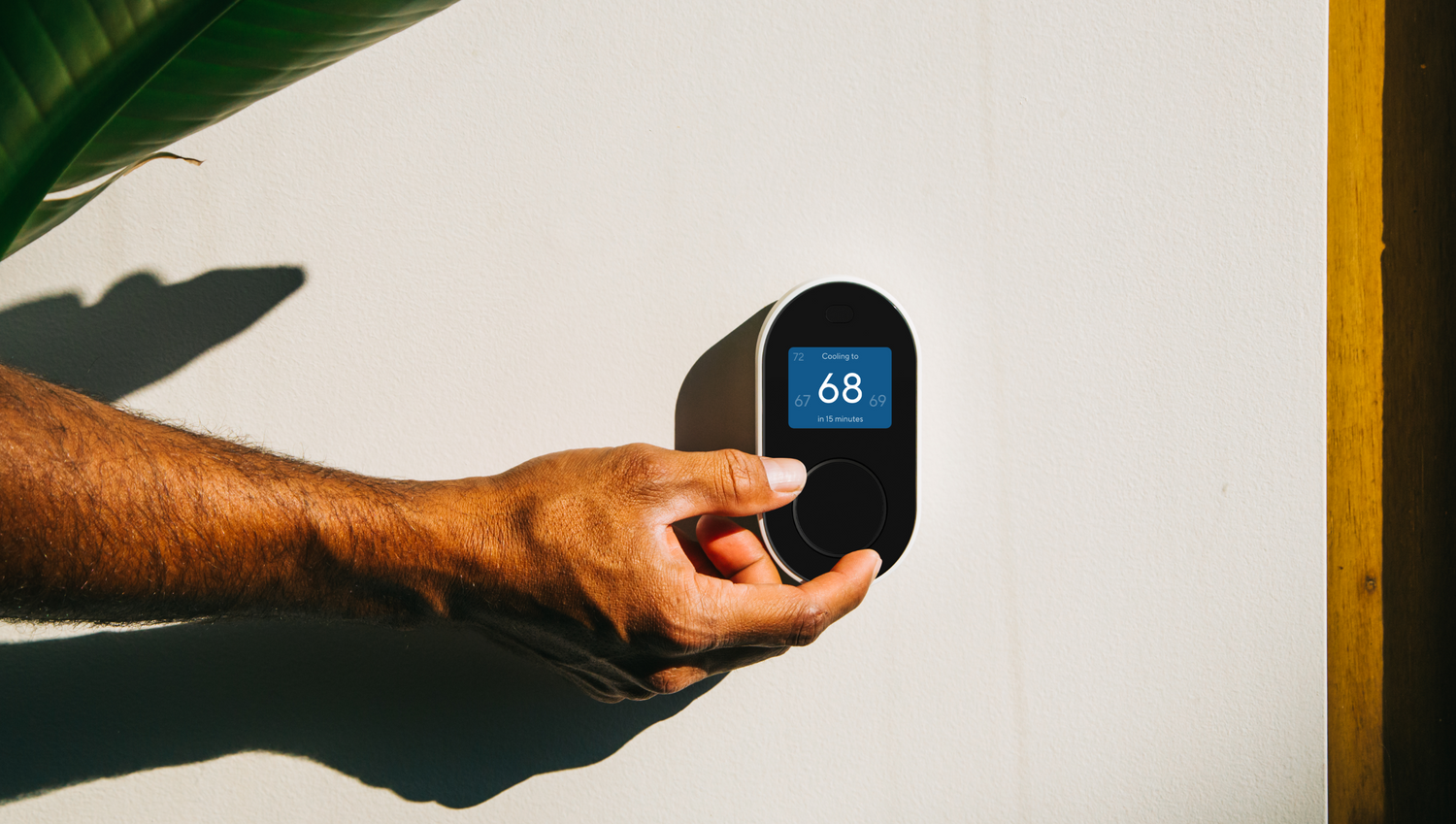 Hand adjusting the Wyze Thermostat unit that is mounted on a wall