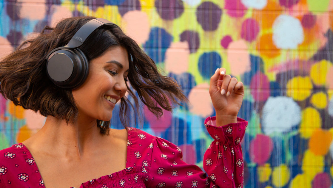 A woman wearing headphones and dancing in front of a colorful mural.
