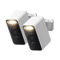  Two white Wyze Battery Cams shown at an angle with its spotlight illuminated and wall mount attached.