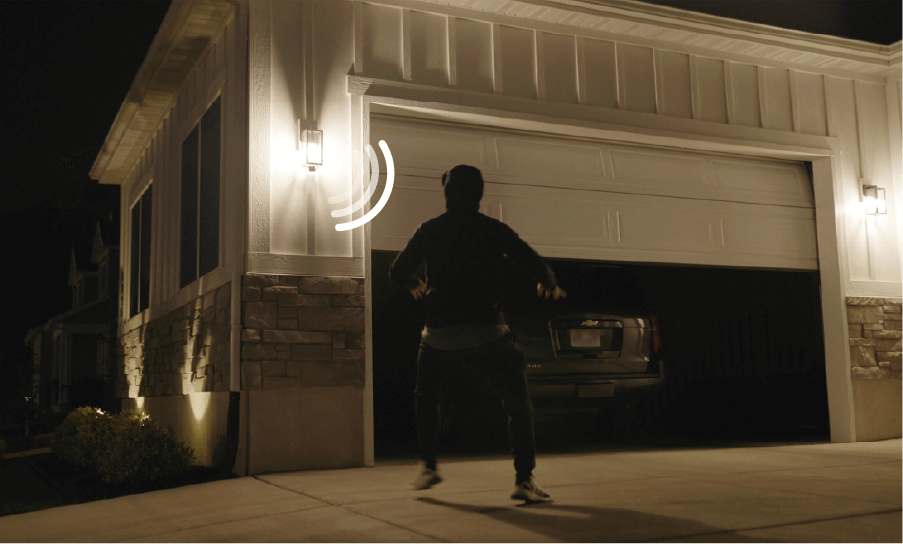 Motion sensor light illuminating driveway with a person approaching a car in a garage at night.