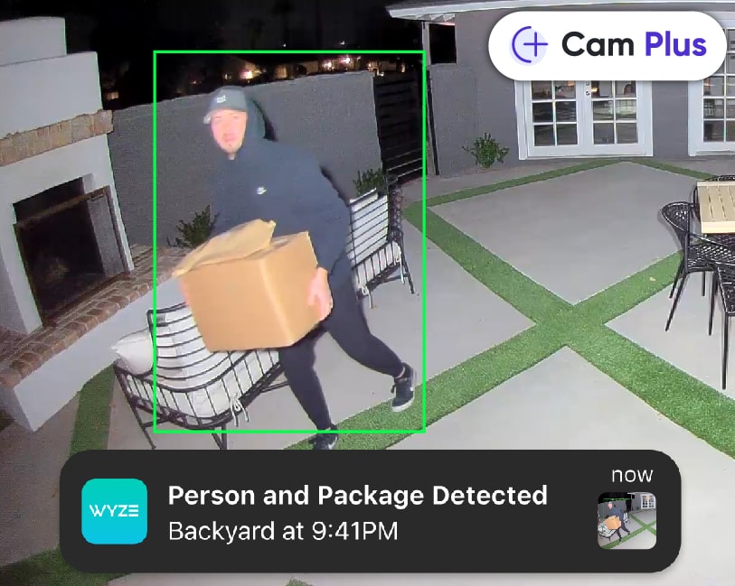 Man carrying packages away from the house during the night with the lights shining directly at him. Phone notification overlay of alert about the camera's detection.