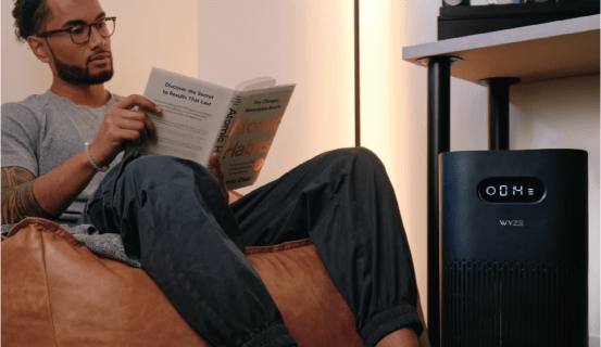 Man reading a book while sitting on a chair with an air purifier nearby