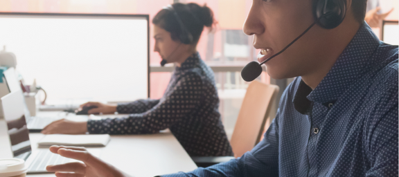24/7 security agent with a headset and is seated in front of a computer.