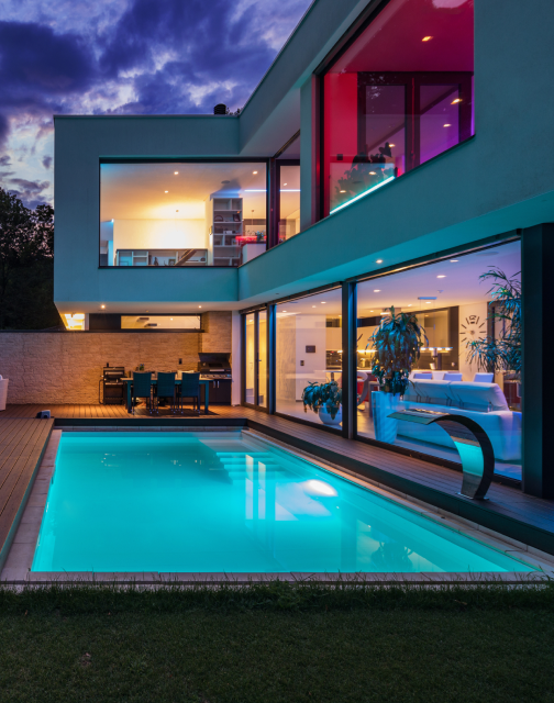 Outdoor view of house with pool. All indoor and outdoor lights are turned on