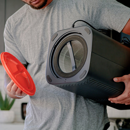 Man holding Air Purifier upside down with one arm and holding the bottom of the Air Purifier with other hand, showing air filter inside.