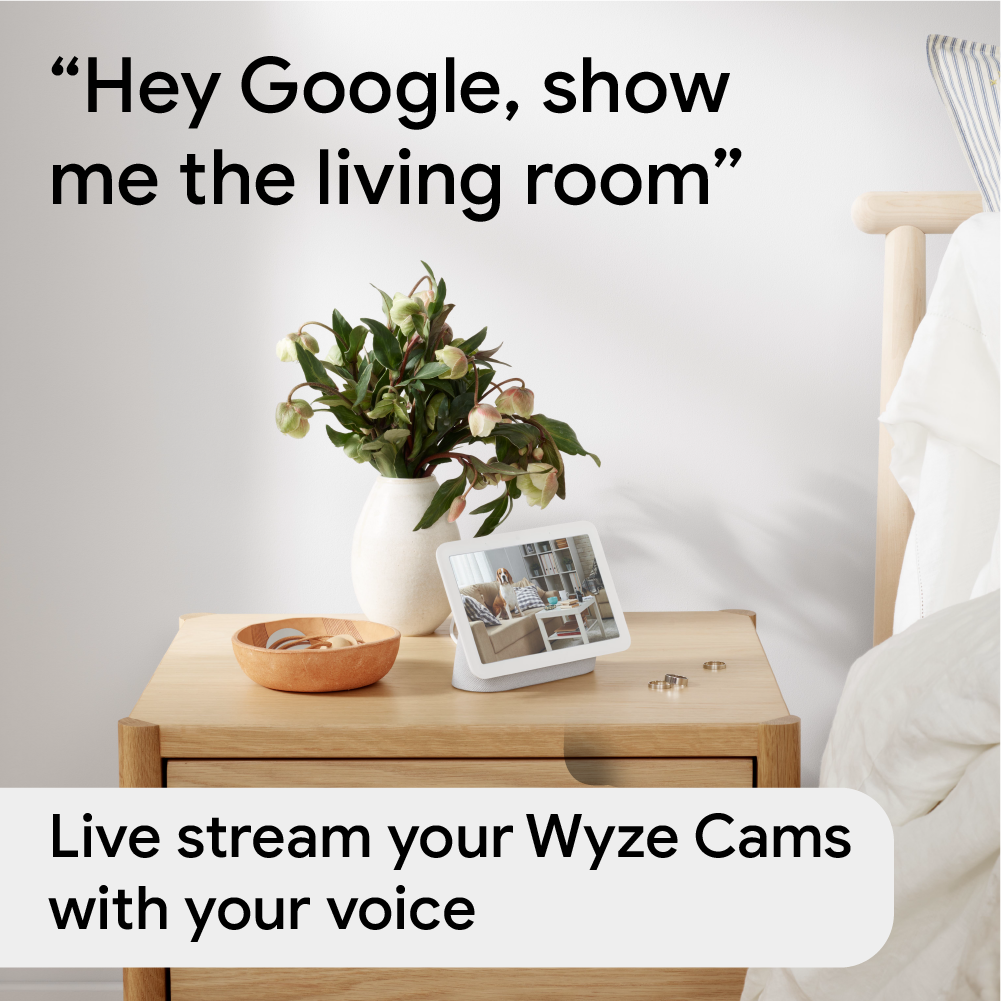 Google Next HUb on a night stand in a bedroom. Text overlay that says "Live stream your Wyze Cams with your voice."