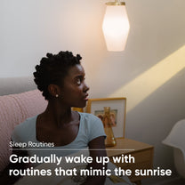 A woman sitting on a bed with a Wyze Bulb White on the nightstand.